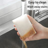 A hand is holding a translucent cleaning sponge under a faucet, demonstrating its ability to wash away stains.