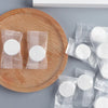 Several sealed packets of white portable compressed cleansing towels are arranged on a wooden plate.