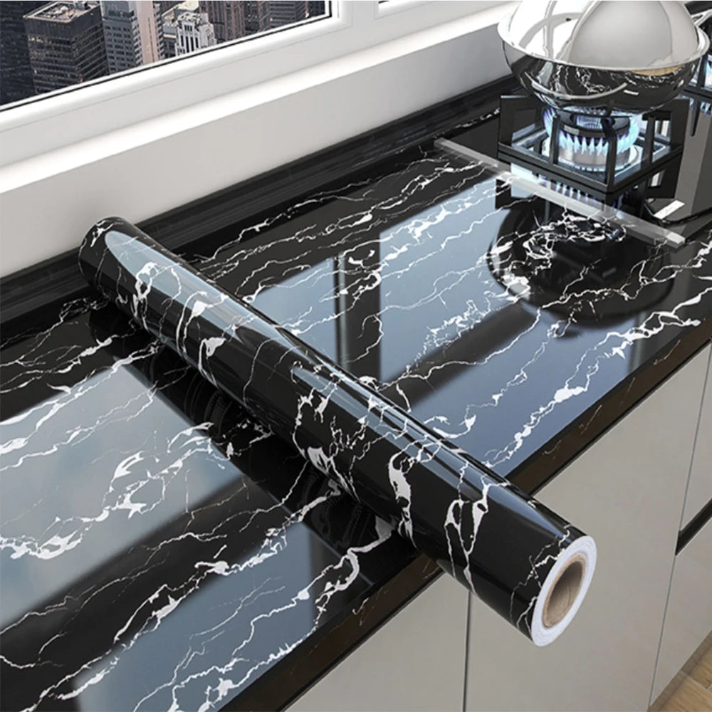 Roll of black marble peel-and-stick film displayed on a kitchen countertop with a stovetop.