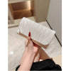 A hand holds an elegant patent leather clutch bag with a chain strap, featuring vertical pleats and a red accent.