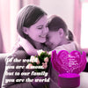 A woman lovingly embraces a child, with a pink heart-shaped LED night light in the foreground.