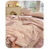 A pink cartoon pattern kids lightweight summer quilt draped on a bed with a fireplace mantel in the background.