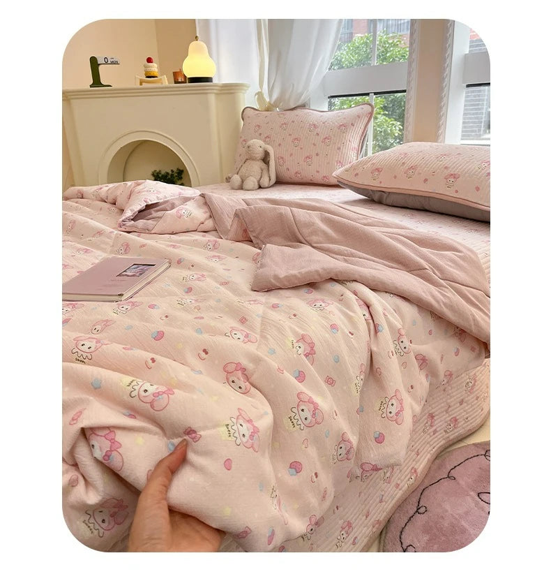 A pink cartoon pattern kids lightweight summer quilt draped on a bed with a fireplace mantel in the background.