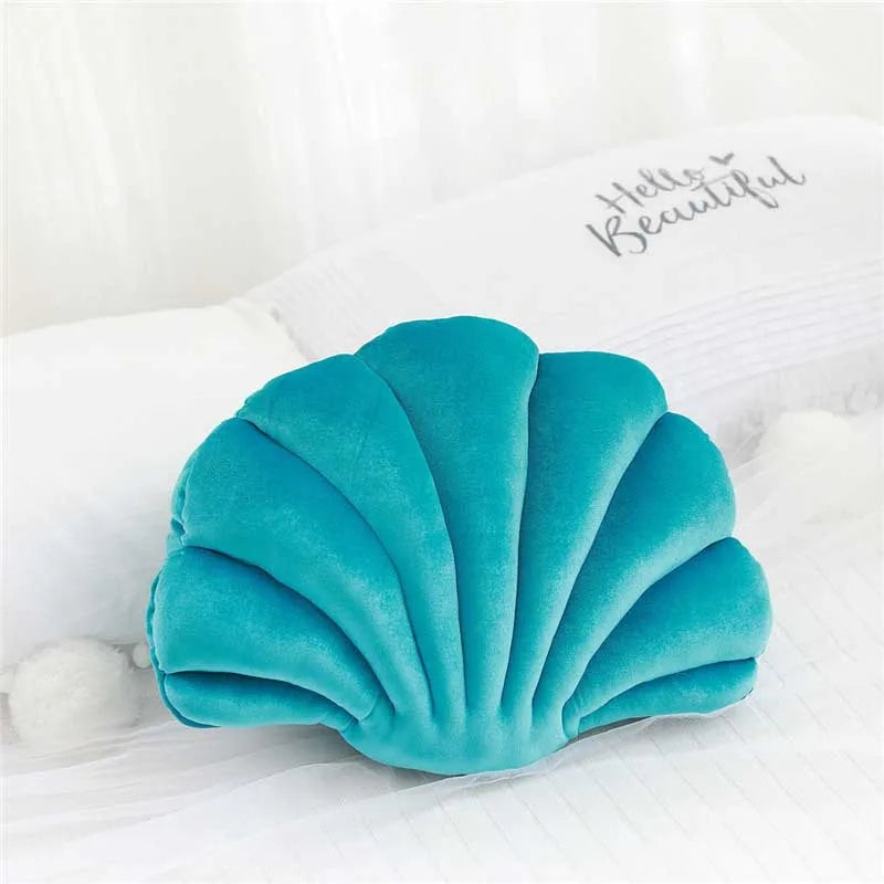 A teal velvet shell print decorative throw pillow resting on white bedding.
