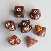 A collection of seven polyhedral dice in various shades of amber and brown resting on a white surface.