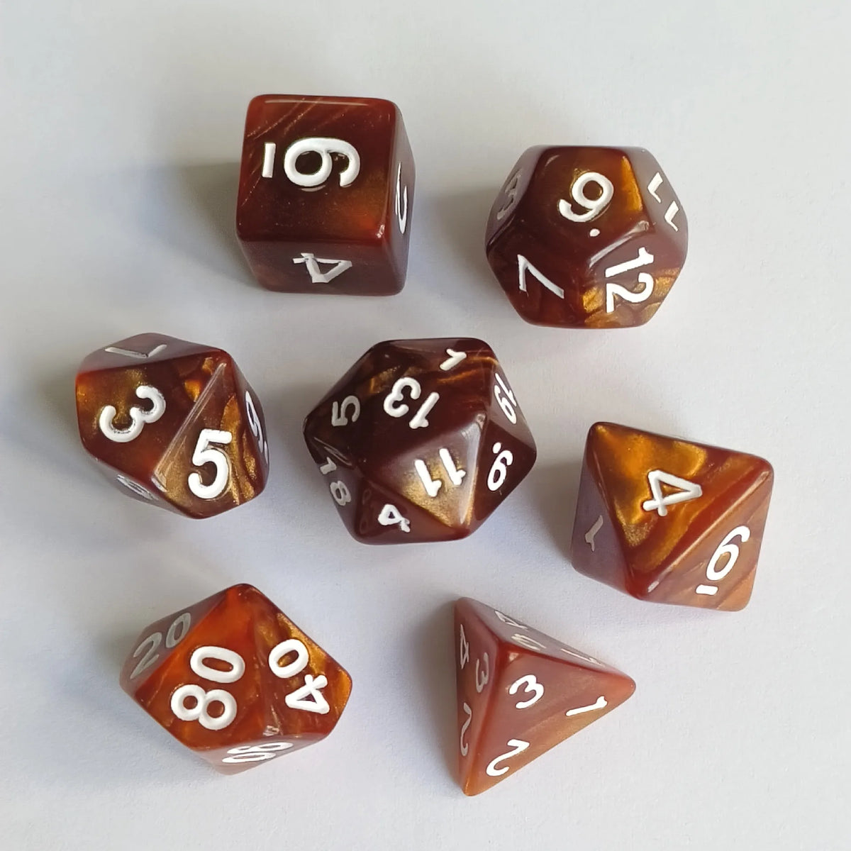 A collection of seven polyhedral dice in various shades of amber and brown resting on a white surface.