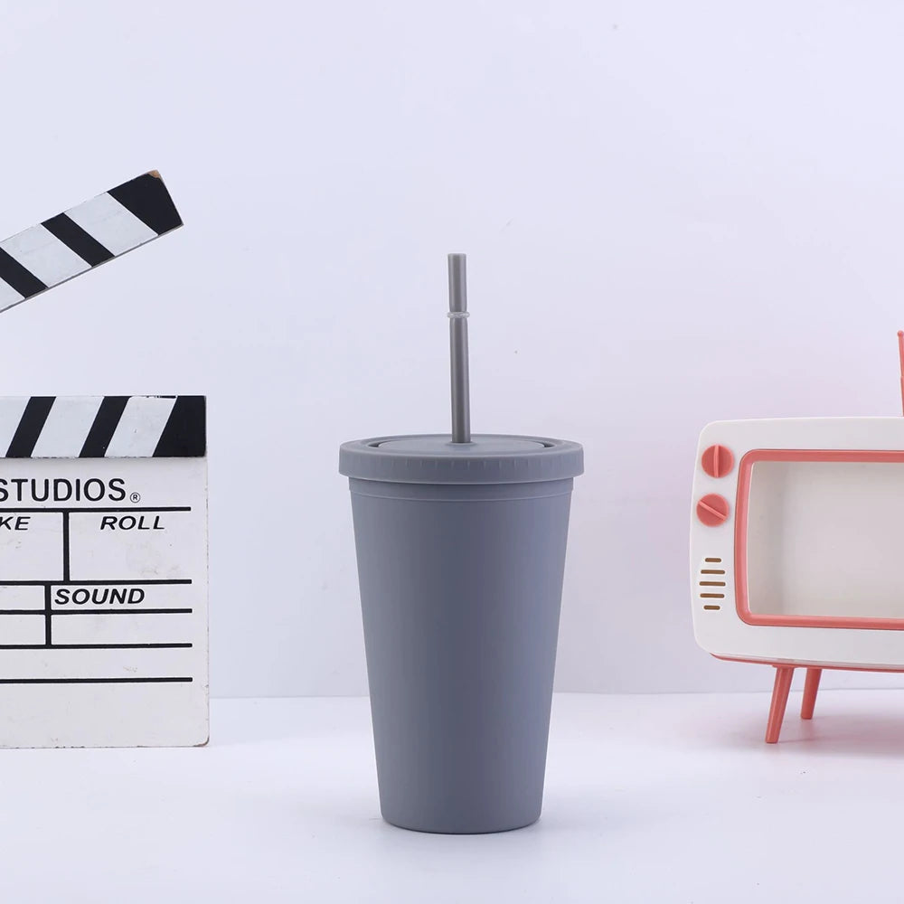 Un tumbler gris avec couvercle et paille, à côté d'un mètre ruban noir et blanc rayé et d'un appareil électronique blanc.