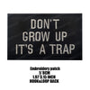 Black embroidered patch with white text that reads DON'T GROW UP IT'S A TRAP