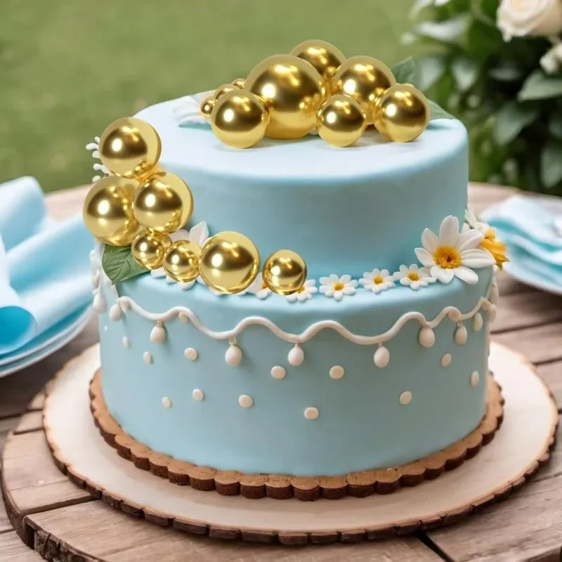 Zwei-stöckiges hellblaues Kuchen mit goldenen Kugendekorationen und weißen Blumenakzenten