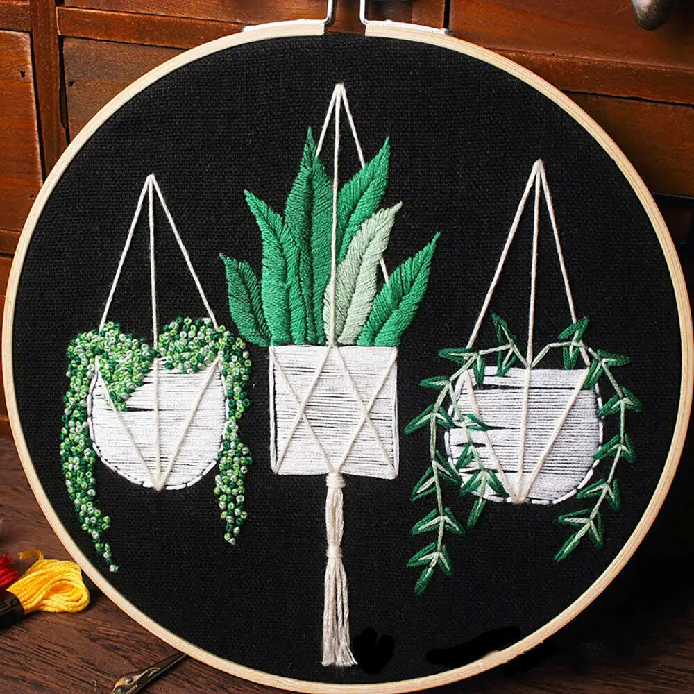 Floral cross stitch embroidery kit featuring three potted plants suspended by twine on a black fabric background