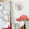 A close-up of a framed abstract artwork with swirling lines, displayed on a white hexagonal wall next to a gold-framed pictur
