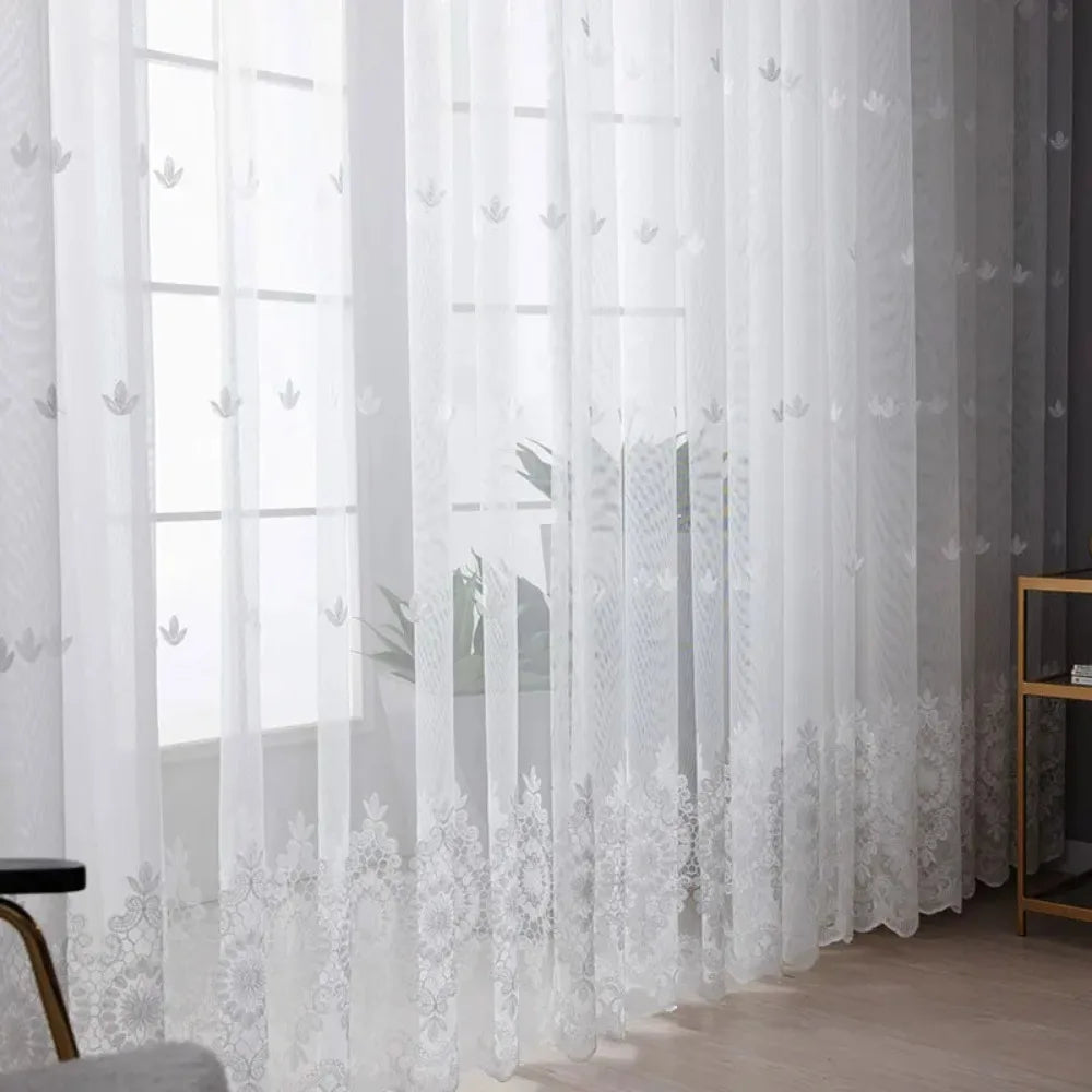 White sheer voile curtain panel with delicate silver embroidery hanging in a window.