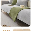 A light gray sofa is covered with a moss green non-slip fabric and features decorative pillows and a tea cup.
