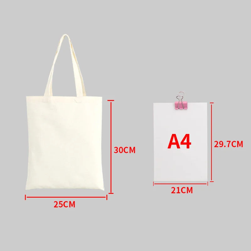 A white canvas shopping tote bag with handles shown next to an A4 sized piece of paper.