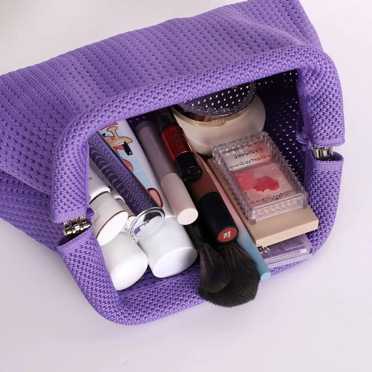 A purple hand-knit clutch bag is open, revealing various makeup and beauty tools inside.