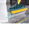 A close-up view of a teal and yellow 2-in-1 floor scrub brush with a squeegee and long handle being used on a glass floor.
