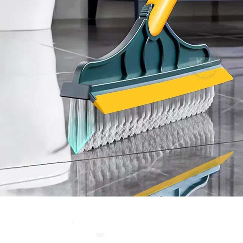 A close-up view of a teal and yellow 2-in-1 floor scrub brush with a squeegee and long handle being used on a glass floor.