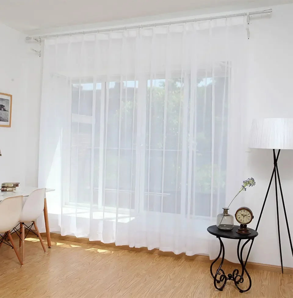 Durchscheinende weiße Tüllvorhänge bedecken ein Fenster, wobei natürliches Licht durchfiltert.