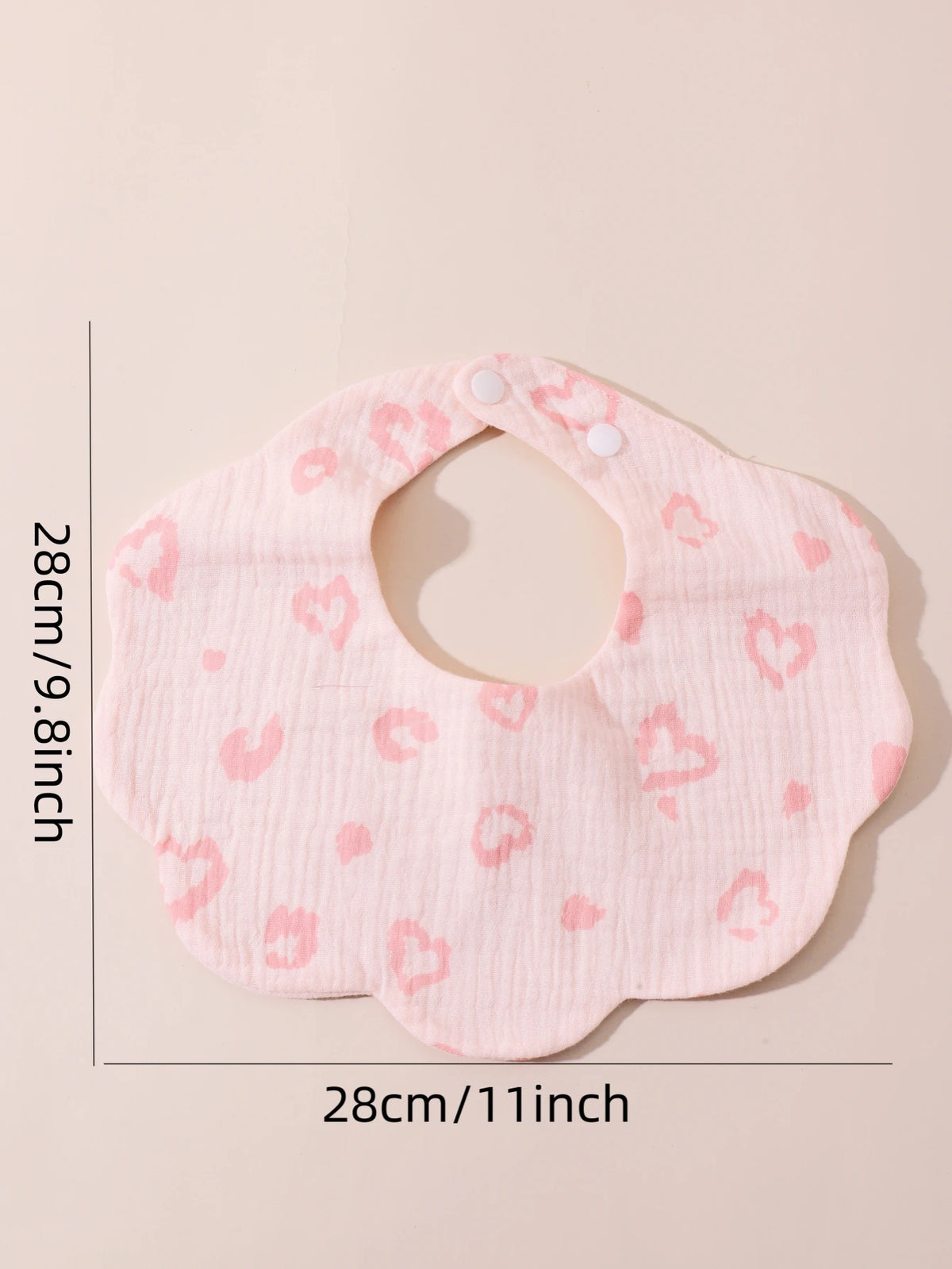 A pink soft cotton baby bib with a ruffle trim and heart pattern, shown flat.
