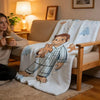 A person is sitting on a sofa with a white blanket featuring a cartoon bear character and trees.