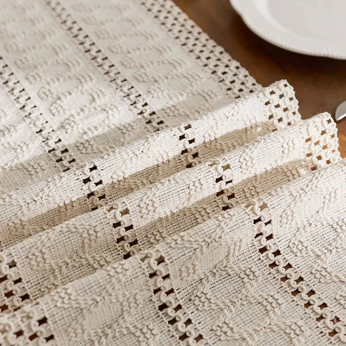 A beige boho table runner with hand-woven tassels and lace trim, shown in a close-up view.