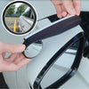 A hand is installing a black carbon fiber blind spot mirror with a rain shield onto a white car's side mirror.