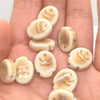 A collection of handcrafted ceramic fish beads in natural beige and cream tones resting on a hand.