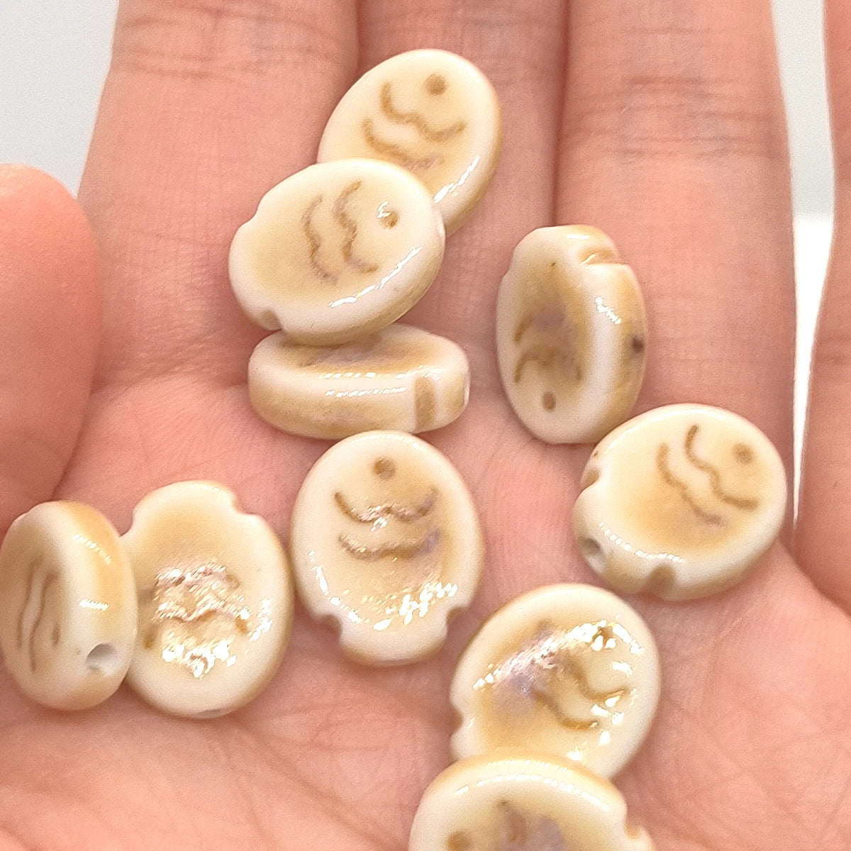 A collection of handcrafted ceramic fish beads in natural beige and cream tones resting on a hand.