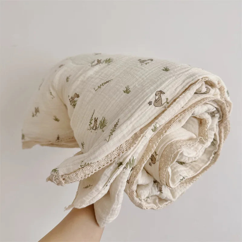 A rolled floral muslin baby blanket in off-white with subtle green embroidery being held by a hand.