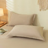A set of solid beige fitted bed sheets and pillowcases displayed on a light-colored bed.