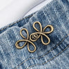 A gold-toned clover buckle attached to a denim jean pocket.