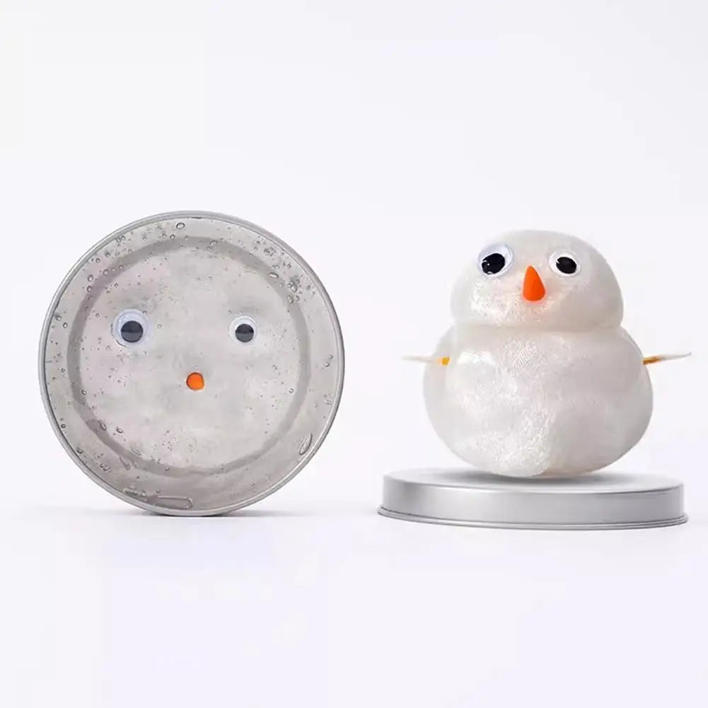 A white, fluffy snow owl figure sits on a silver tin, next to the clear storage tin.
