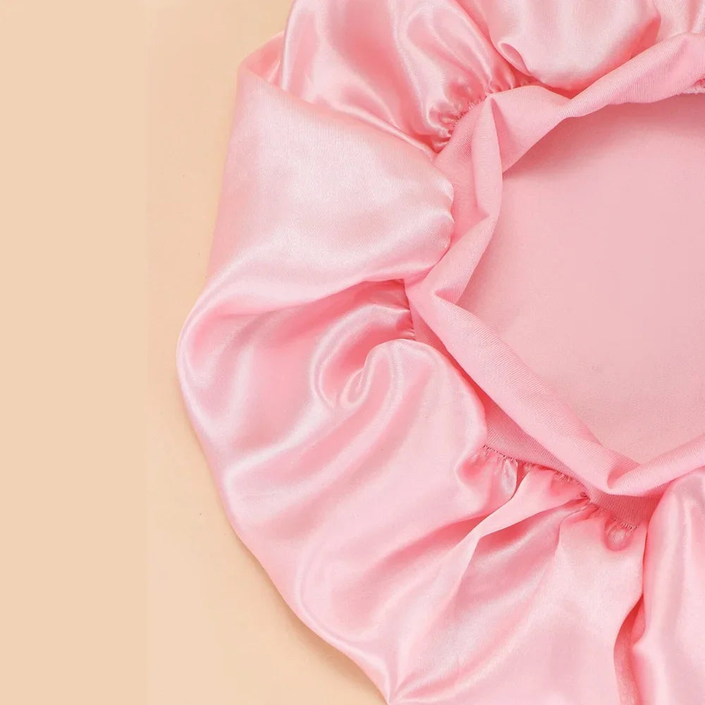 Pink satin wide brim shower cap draped softly on a neutral background.
