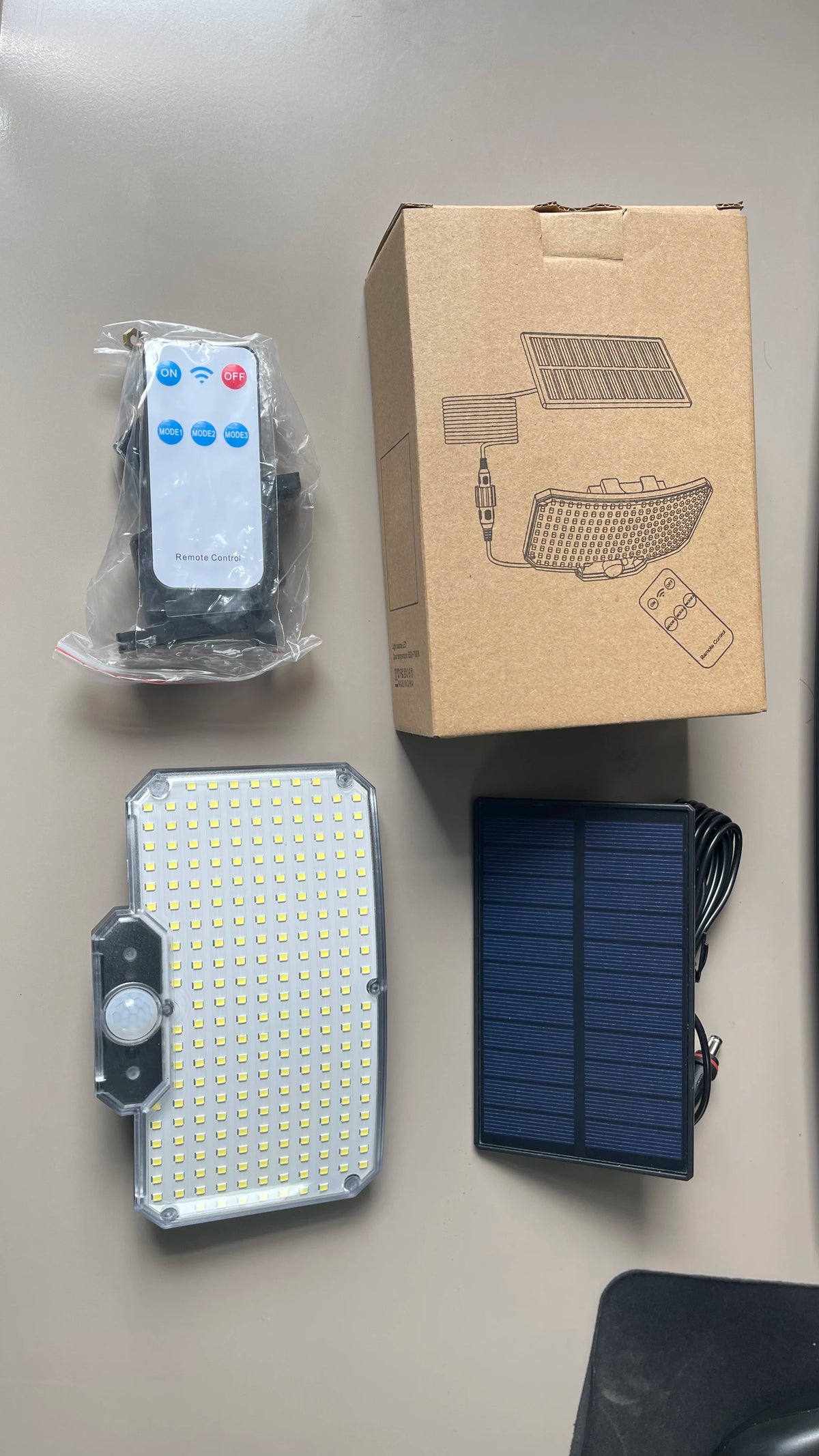 A box containing a solar-powered motion sensor security flood light, a remote control, and a standalone solar panel.