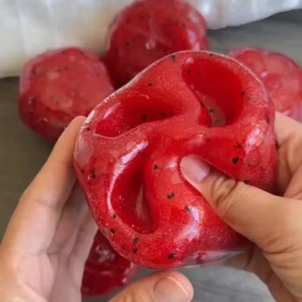 Une main tient un jouet anti-stress en slush de pastèque rouge vif sur un arrière-plan flou d'articles similaires.