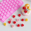 A pink silicone mold tray filled with small heart-shaped silicone molds in various shades of pink and red.