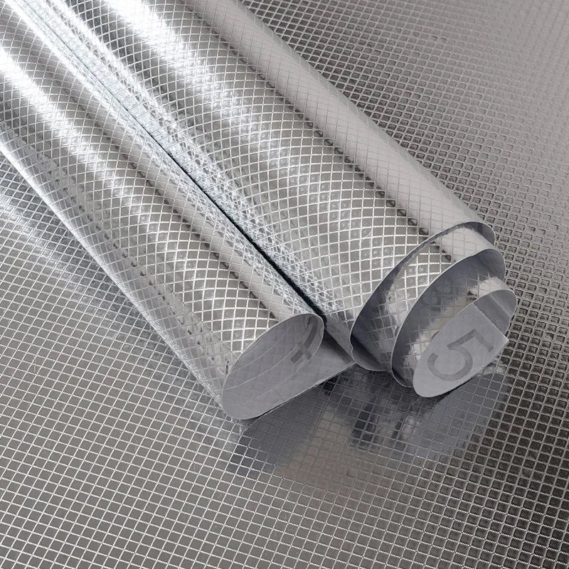 Roll of silver aluminum foil kitchen backsplash sticker being rolled up on a textured surface.
