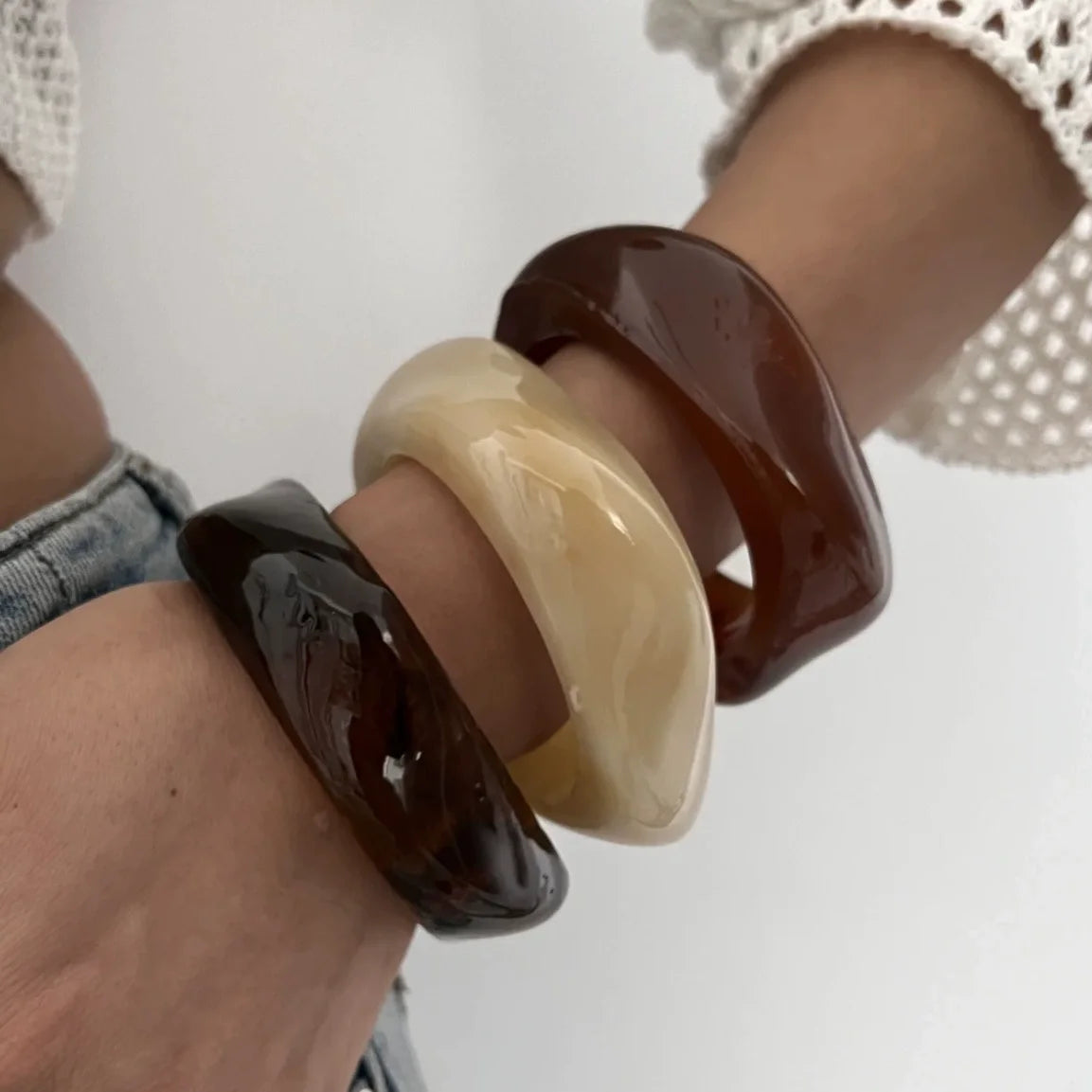 Gros plan d'une main portant une pile de bracelets de poignet acryliques géométriques vintage aux tons ambre et marron.