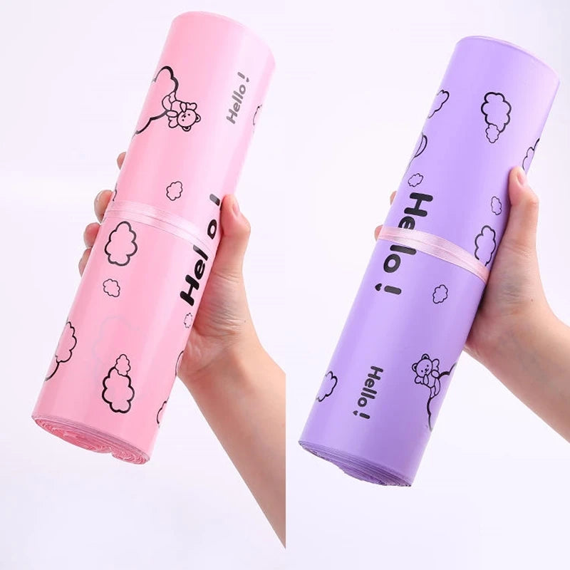 A hand holds a purple self-sealing mailing bag featuring a white Hello bear design.