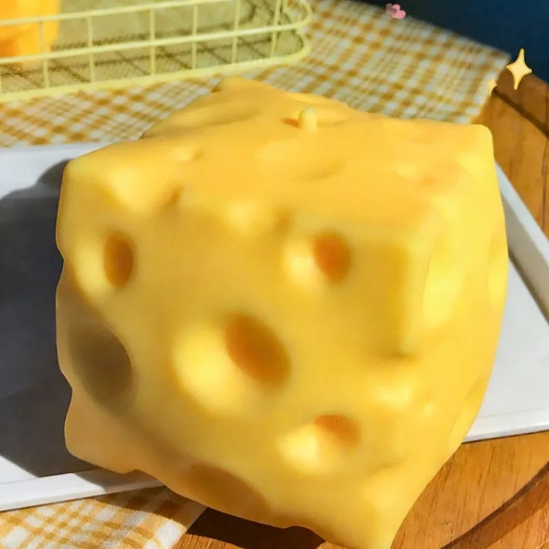 A large, yellow, squishy cheese-shaped fidget toy resting on a white plate.