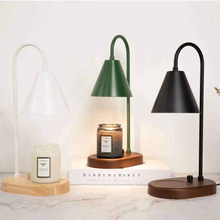 A black electric candle warmer lamp with a green shade and wooden base sits on a white marble surface.
