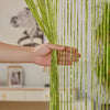 A hand touches a vertical curtain made of thin, bright lime green tassels hanging down.