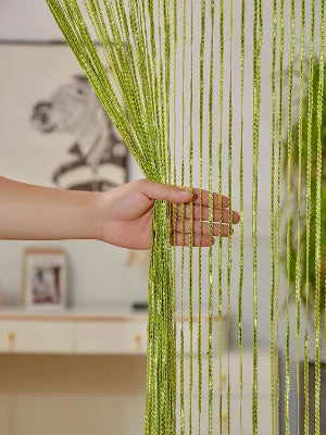 A hand touches a vertical curtain made of thin, bright lime green tassels hanging down.