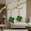 Gold branch keychain charm with a green four-leaf clover hanging in front of a light gray sofa.