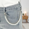 A silver pearl and gold chain purse hanging from the pocket of light gray denim jeans.