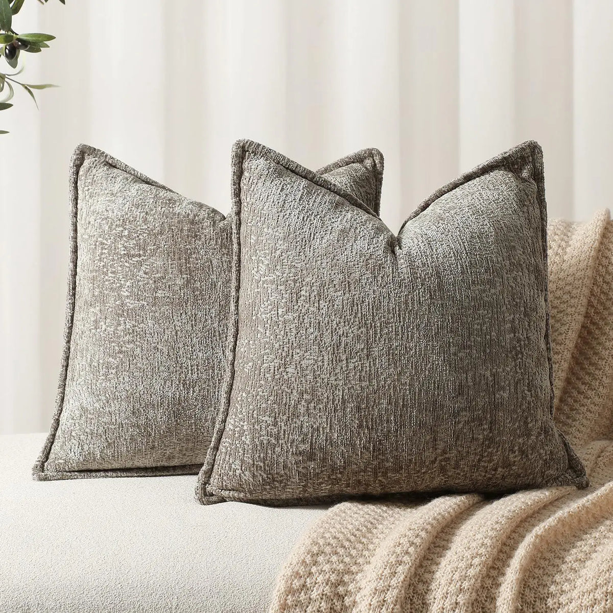 A close-up of a square gray chenille decorative cushion cover resting on a beige knitted fabric.