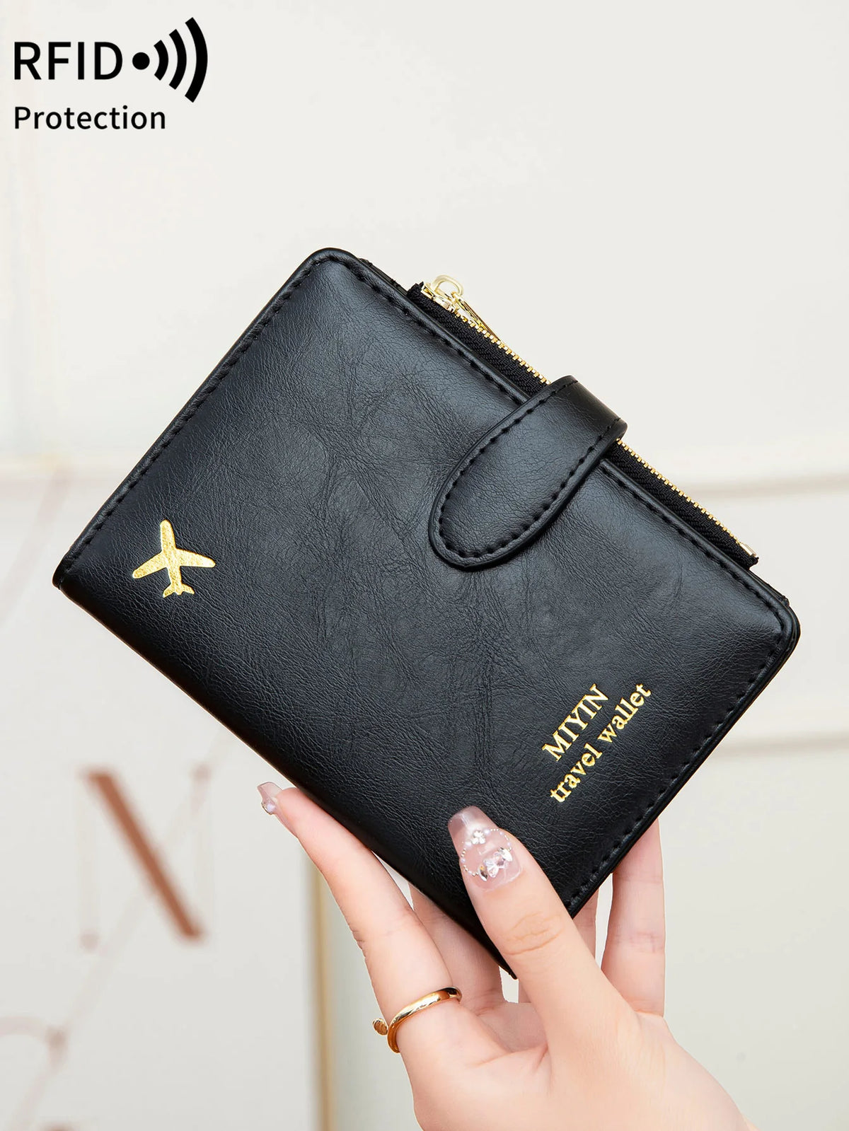 A hand holds a black leather travel wallet with a gold zipper and an airplane pattern, designed for RFID protection.