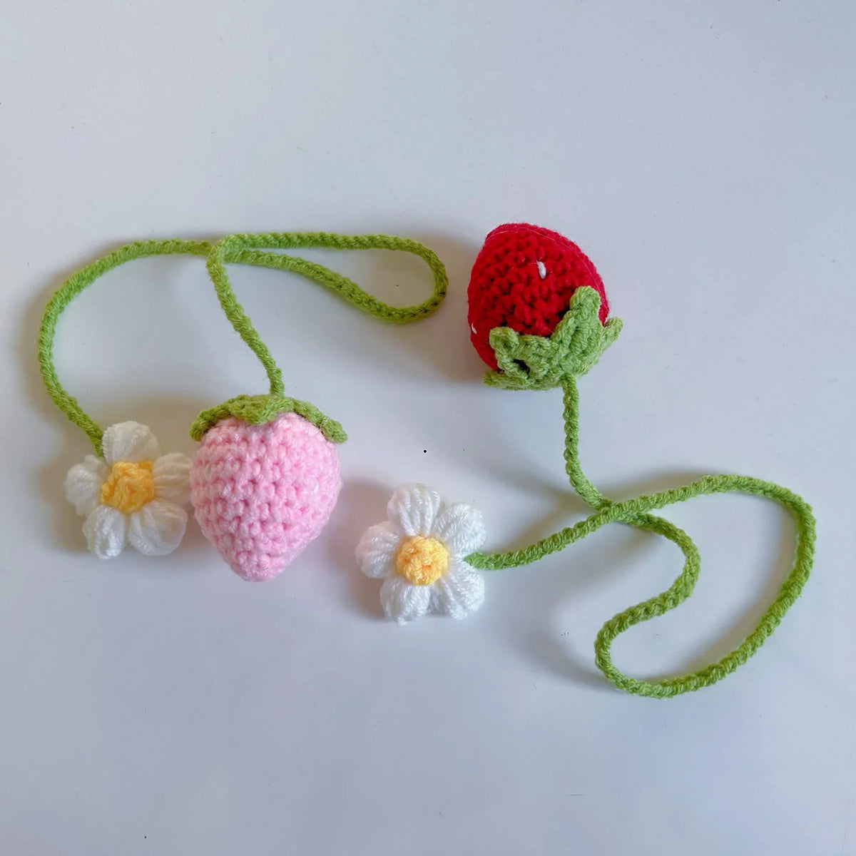 Handmade crochet strawberry with a green stem and leaves, next to a white flower.
