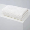 A white, textured bath towel folded neatly on a white surface.