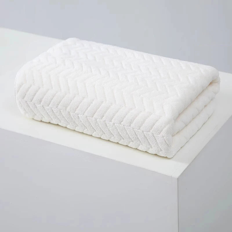A white, textured bath towel folded neatly on a white surface.